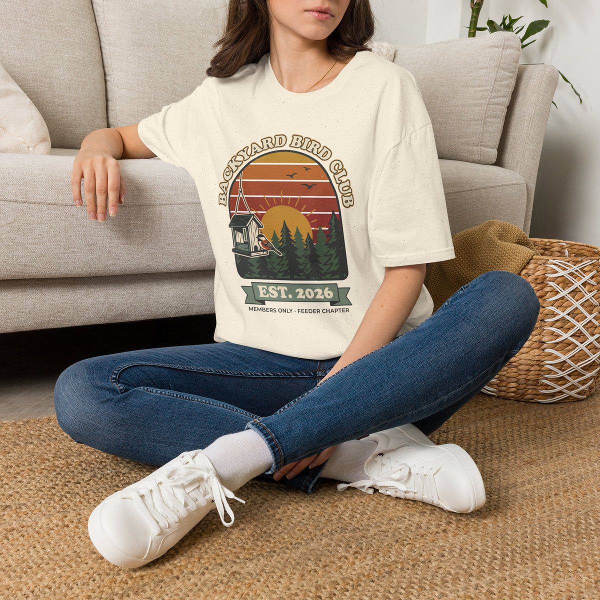 T-shirt with retro 'Backyard Bird Club Est. 2026' badge design featuring a sunset, pine trees and a chickadee at a bird feeder