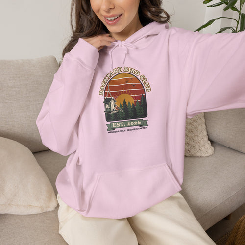 Hoodie with retro 'Backyard Bird Club Est. 2026' badge design featuring a sunset, pine trees and a chickadee at a bird feeder