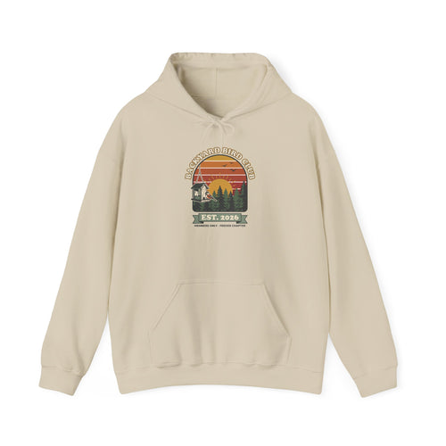 Hoodie with retro 'Backyard Bird Club Est. 2026' badge design featuring a sunset, pine trees and a chickadee at a bird feeder
